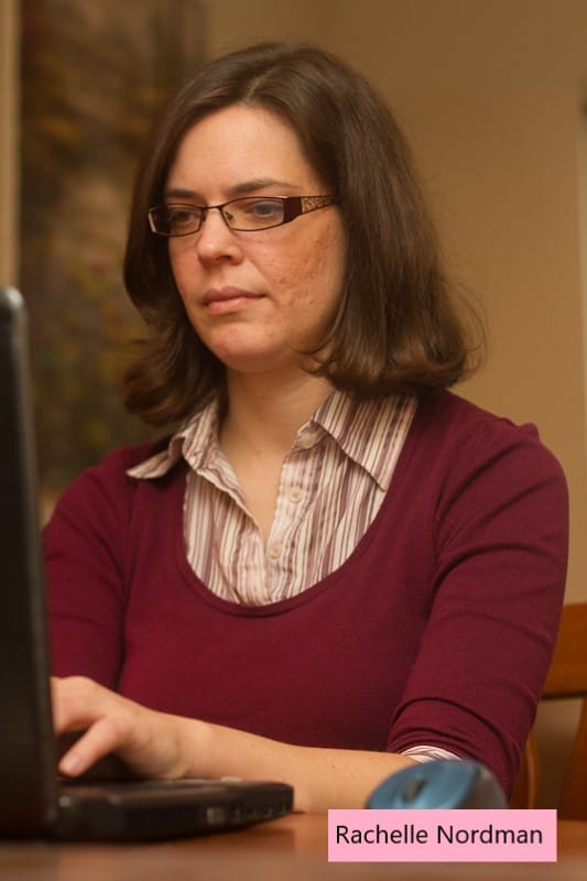 woman in maroon sweater with brown shoulder length hair typing on a laptop with a serious expression