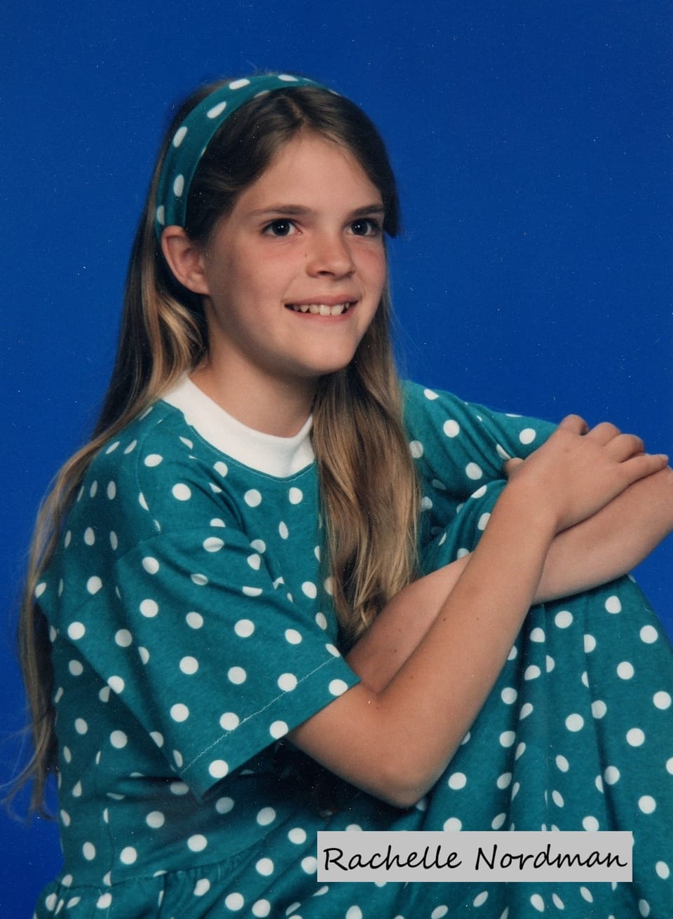 studio portrait of a young girl seated in a green polka dot dress and long hair